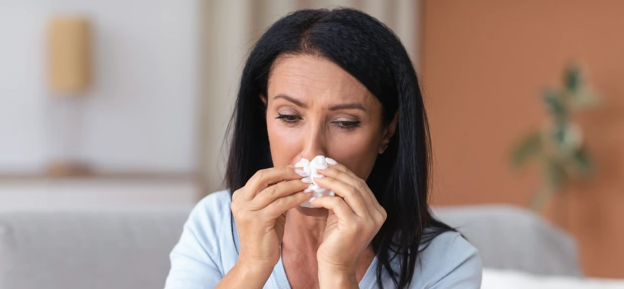 Here's an alt tag for the image: Woman blowing her nose with tissue.